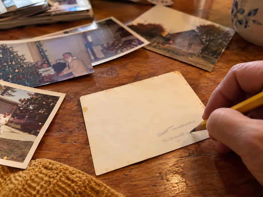 A pencil writing softly near the edge of the back of an old family photo on a wooden table, with the handwriting blurred and unreadable