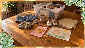Baby shoes, old report cards, a crayon drawing and a macaroni card spread across a kitchen table beside a plastic keepsake bin