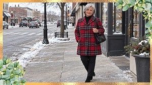 Woman over 50 in a red plaid wool winter coat walking down an ordinary small-town main street