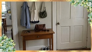 A small wooden table by a back door with keys, a purse and sunglasses, and three wall hooks holding a jacket, a tote bag and a shoulder bag