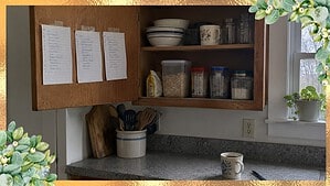 Three handwritten lists taped inside an open kitchen cabinet door, with a cup of coffee and a pen on the counter below