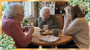 Three women of different ages sharing coffee and conversation around a small kitchen table.