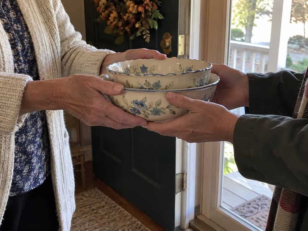 A woman handing a set of pretty serving bowls to a friend at the front door.