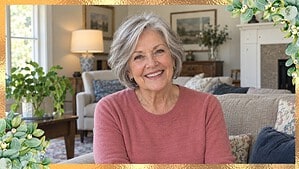 Woman over 70 with a silver-gray short layered bob, smiling in a rose sweater in her living room