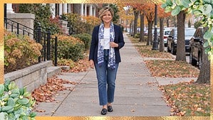 Woman in her 50s wearing a long blue paisley scarf draped over a navy blazer, white tee and jeans on a fall sidewalk
