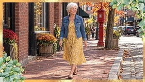 Woman with short white hair in a denim jacket and yellow floral midi dress walking on a brick sidewalk in Portland, Maine
