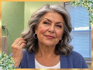 Woman with wavy silver hair smiling after doing her makeup in her bathroom