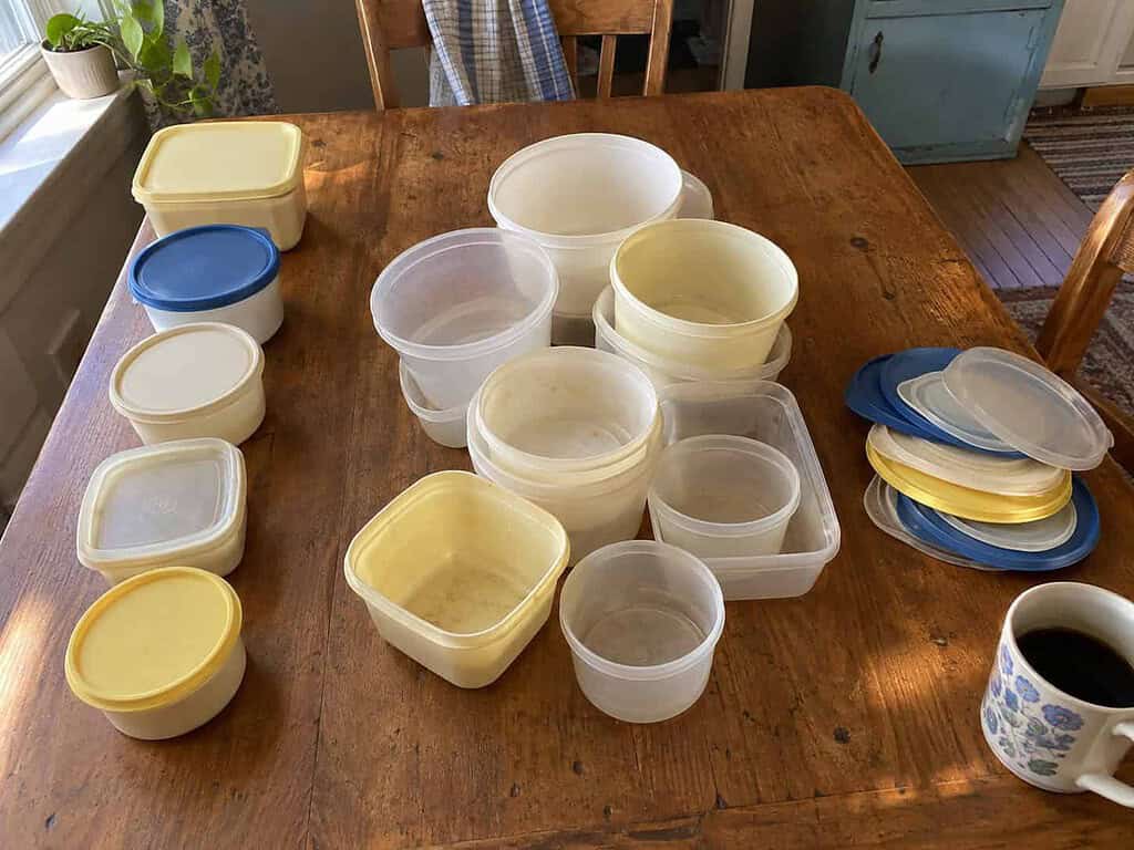 Plastic food containers sorted on a kitchen table into matched sets, bowls with no lids, and lids with no bowls