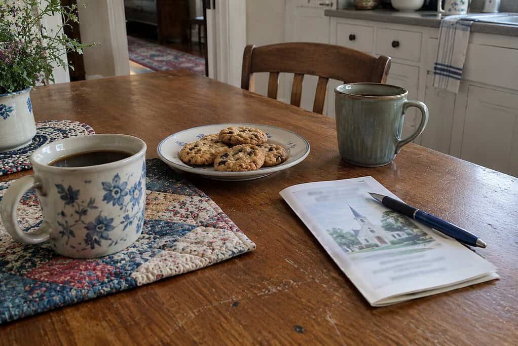 Two coffee mugs, a plate of cookies and a folded church bulletin with a pen on a kitchen table