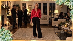Woman over 50 in a red satin blouse, black wide-leg pants and gold flats holding a gold clutch at a New Year’s Eve party