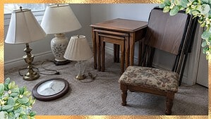 Extra lamps, a wall clock, nesting tables, folded TV trays and a footstool gathered on a spare room floor to sort