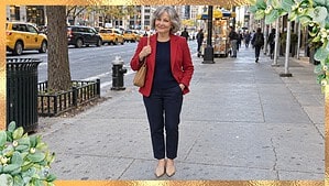 Petite woman in her 60s in a red blazer, navy sweater and navy ankle pants walking on a busy New York City street