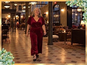 Smiling plus size woman with silver hair in a merlot velvet jumpsuit walking through a hotel lobby