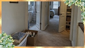 Upstairs hallway with an open bathroom, bedroom and linen closet, and a laundry basket of towels and a box of old bathroom bottles on the carpet