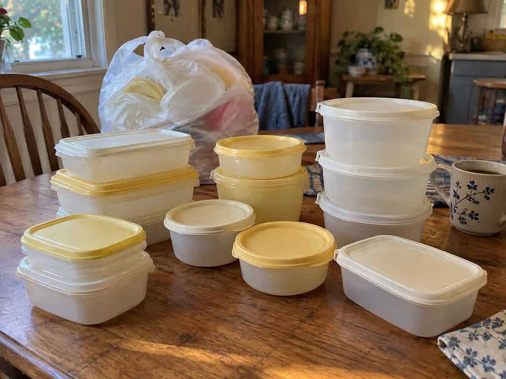 A small set of matched plastic food containers and four larger soup tubs on a kitchen table, with a bag of extras behind them