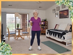Smiling woman with short silver hair doing biceps curls with purple dumbbells in her living room