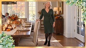 Thanksgiving dinner outfit over 70: silver-haired woman in a green wrap dress and black ankle boots beside a set holiday table