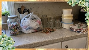 A jar of twist ties, a bag stuffed with plastic bags, rubber bands, glass jars, old margarine tubs and folded wrapping paper on a kitchen counter