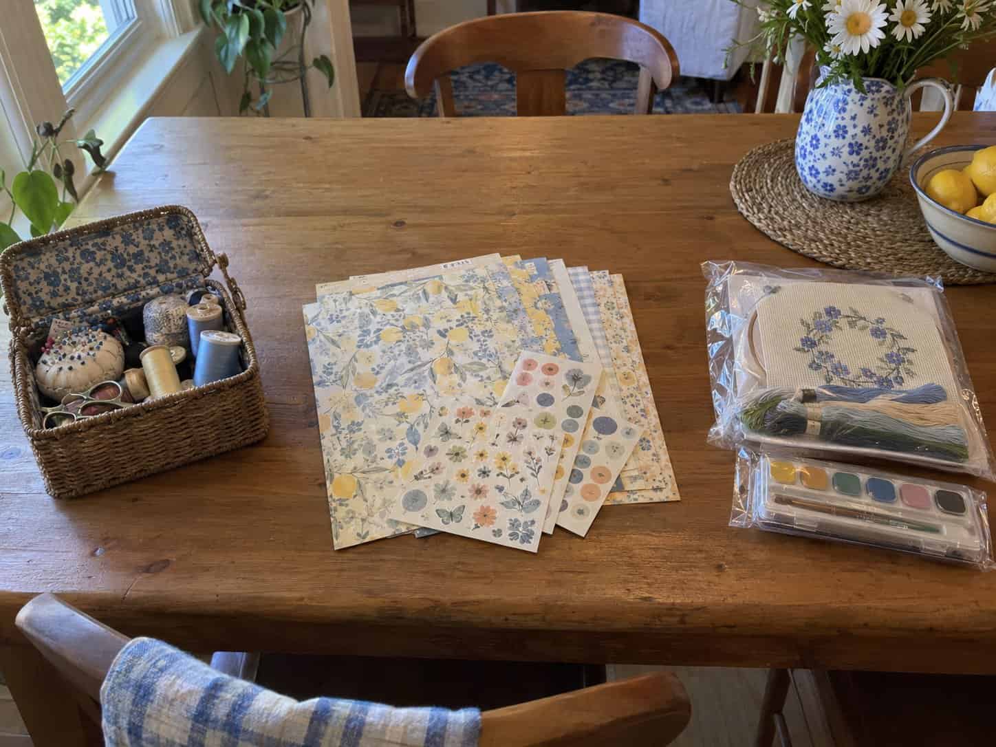 Craft supplies in three groups on a kitchen table: a sewing basket, scrapbook paper and sealed craft kits