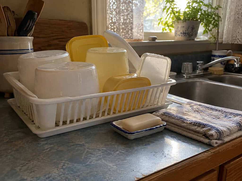 Washed plastic tubs and lids drying upside down in a dish rack beside a kitchen sink